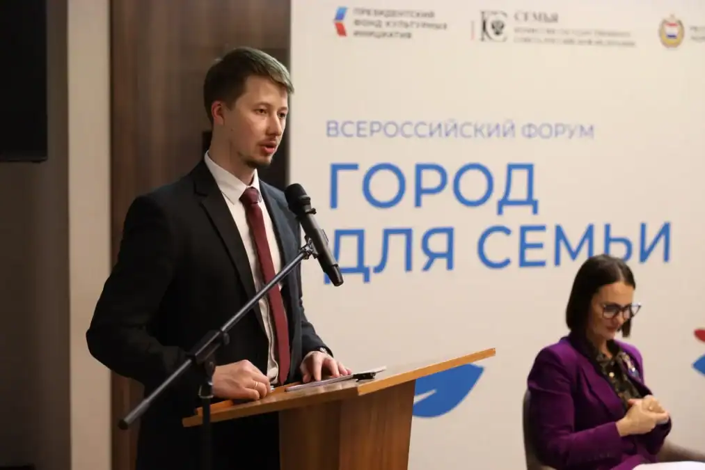 Мужчина выступает с трибуны на фоне баннера форума.
