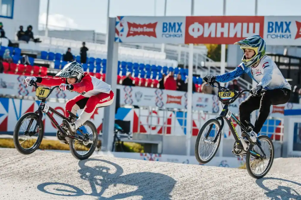Два BMX-райдера едут по трассе под аркой с надписью «ФИНИШ».