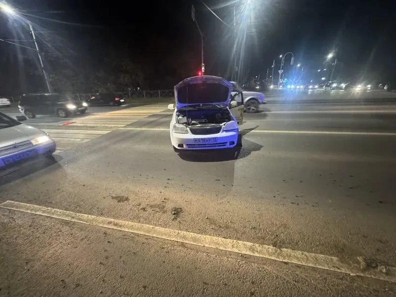 Белый автомобиль с открытым капотом стоит у пешеходного перехода ночью.