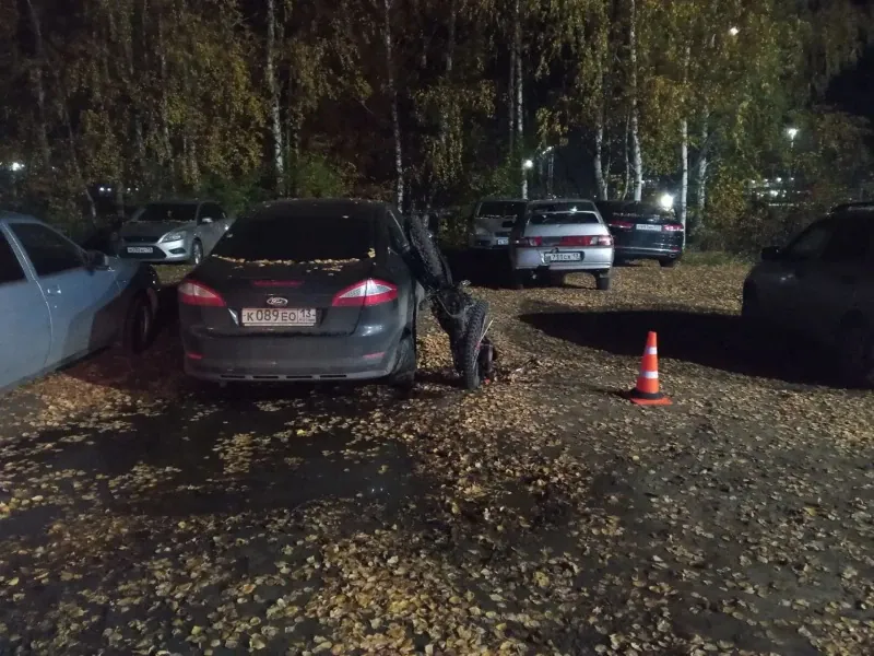 Поврежденный мотоцикл находится у задней части темного седана на парковке.