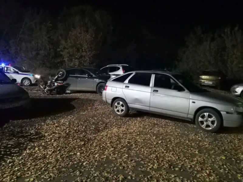 Поврежденный мотоцикл лежит среди припаркованных автомобилей в темноте.