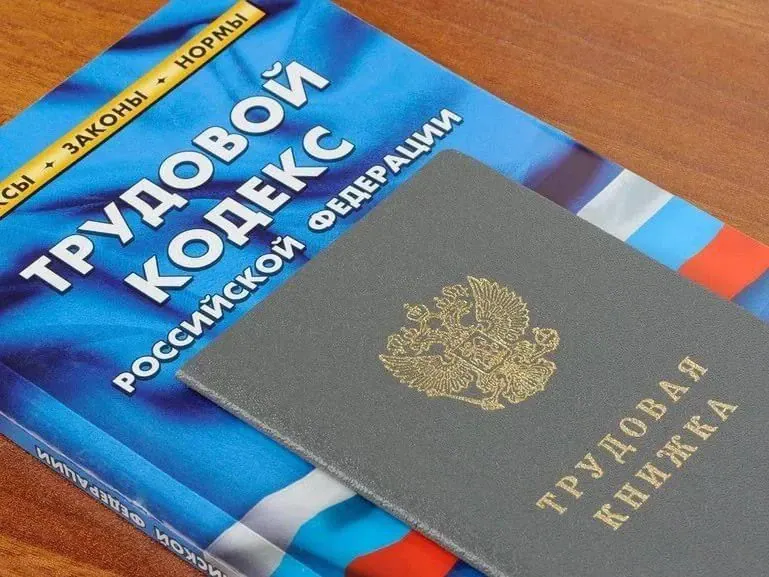 Трудовой кодекс Российской Федерации и трудовая книжка лежат на деревянном столе.