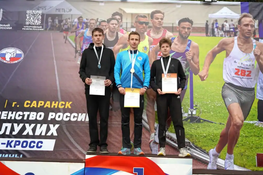 Трое легкоатлетов с медалями и дипломами стоят на пьедестале.