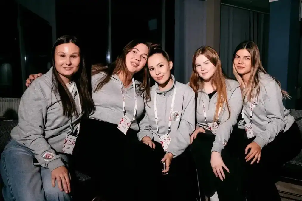 Пять участниц в серых толстовках позируют в помещении семинара.