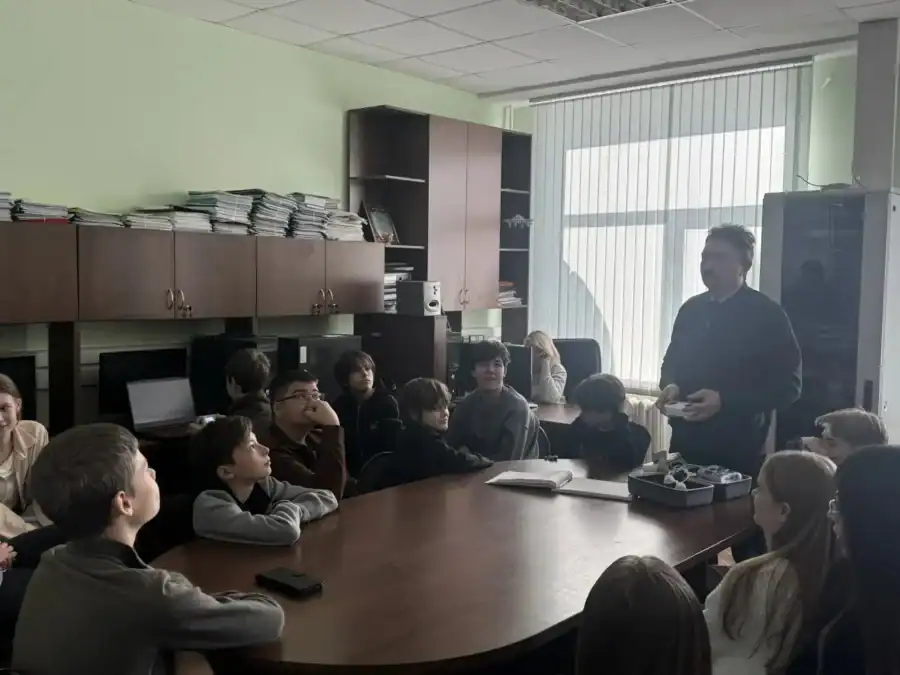 Преподаватель демонстрирует школьникам оборудование для беспилотной авиации в аудитории.