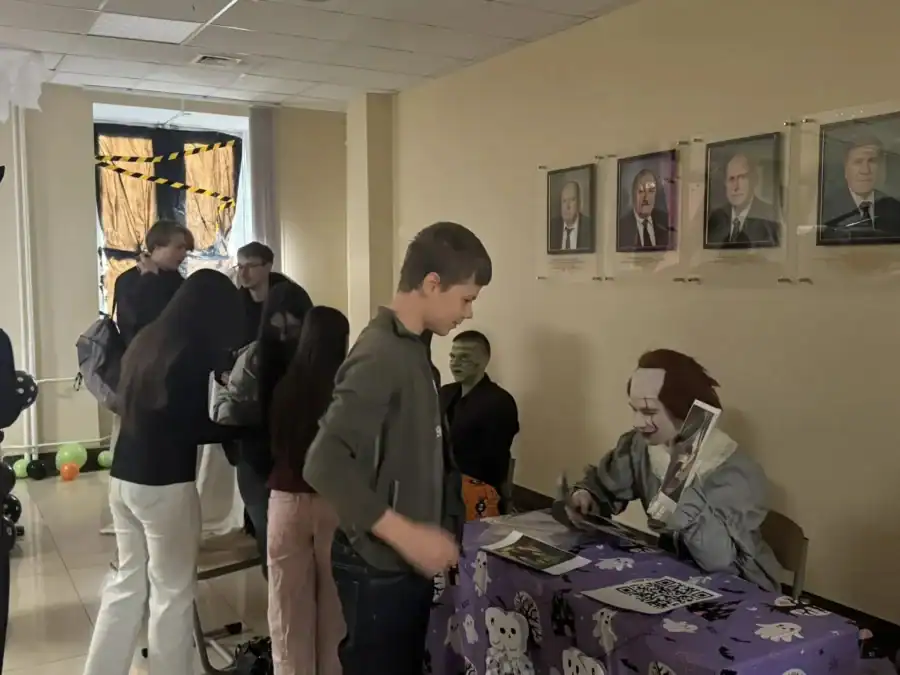 Школьники подходят к столу участников хэллоуинской акции в университетском холле.