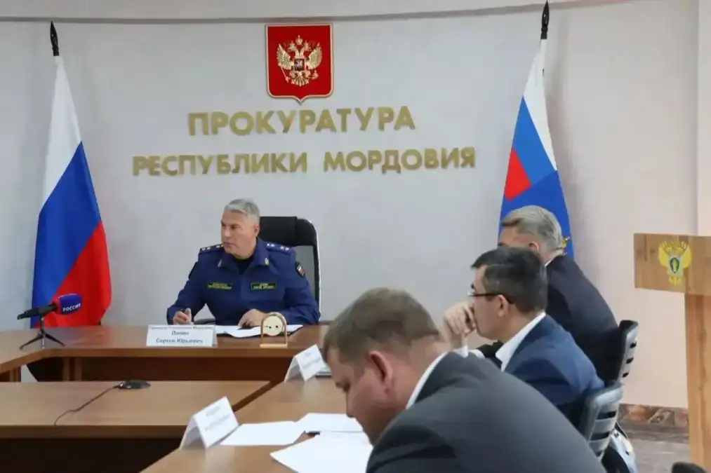 Мужчина в синей форме проводит совещание за столом с представителями ведомств.