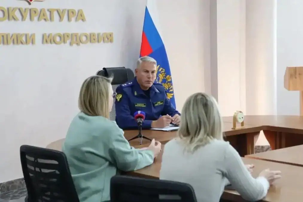 Мужчина в синей форме беседует с двумя женщинами за столом.