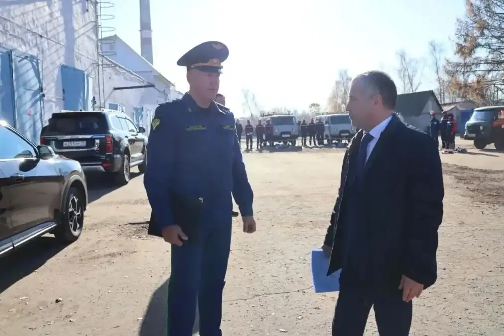 Двое мужчин беседуют на территории производственной базы рядом со служебными автомобилями.