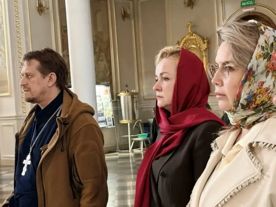 Трое людей в храме стоят во время церковной службы.