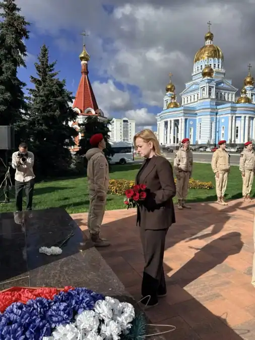 Женщина с красными цветами стоит у мемориала рядом с почётным караулом.