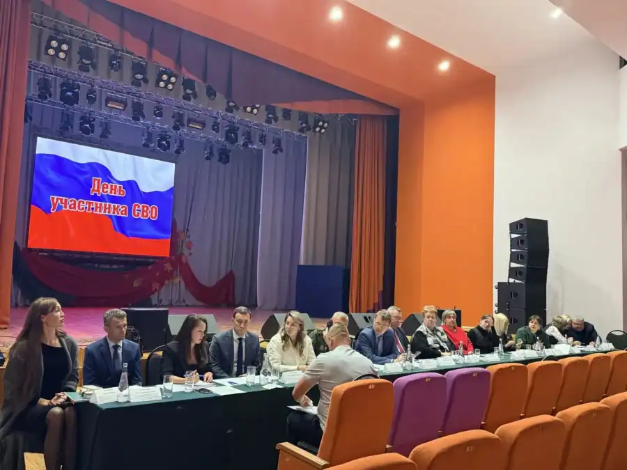 Участники круглого стола сидят в зале перед сценой с экраном.