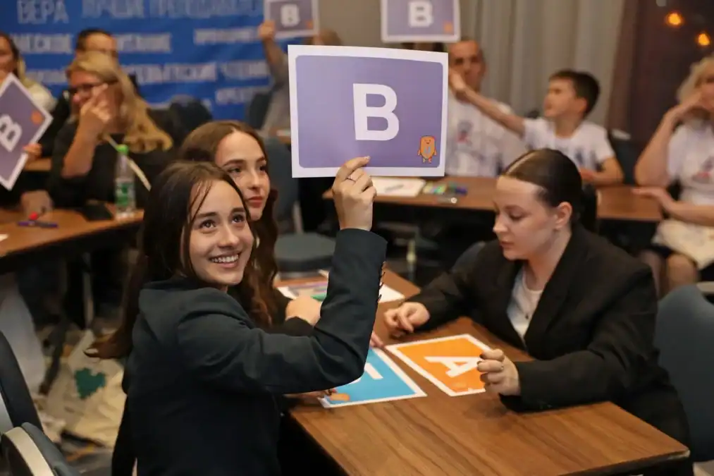 Девушка поднимает карточку с буквой «В» во время командной игры.