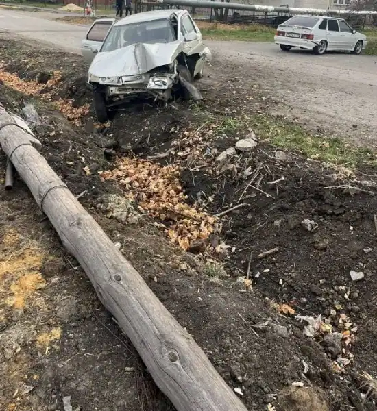 Легковой автомобиль с разбитой передней частью стоит у кювета рядом с упавшей опорой.