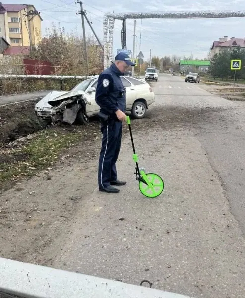 Сотрудник полиции измеряет участок дороги возле повреждённого легкового автомобиля.