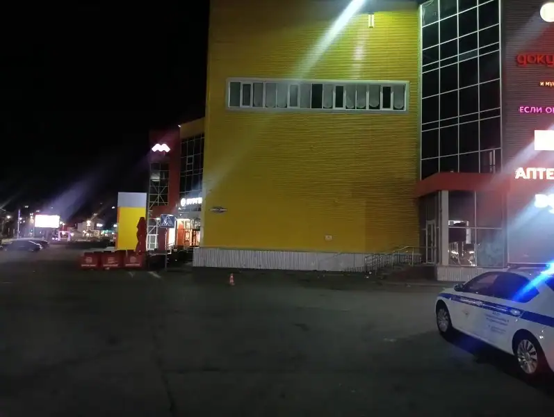 Полицейский автомобиль с включёнными маячками стоит ночью у торгового здания.