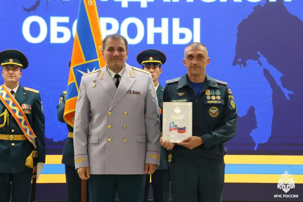 Спасатель в форме держит наградной документ в рамке на сцене.