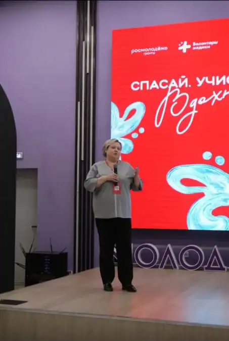 Женщина с микрофоном выступает на сцене перед экраном проекта MedUnity.