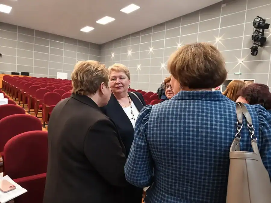 Несколько участниц беседуют между рядами красных кресел в зале.