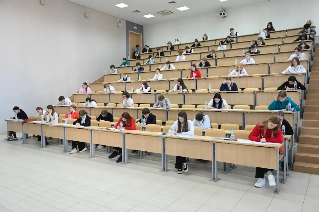 Школьники пишут работы за партами в большой лекционной аудитории.