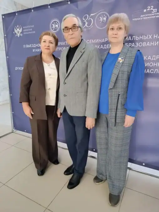 Трое участников позируют перед брендированной стеной научно-практического семинара.
