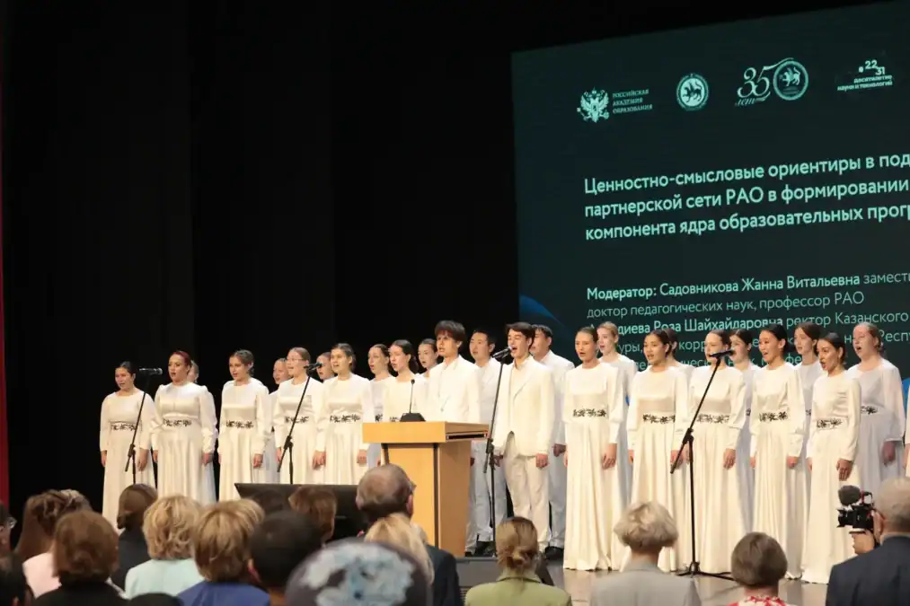 Хор в белых костюмах выступает на сцене перед участниками семинара.
