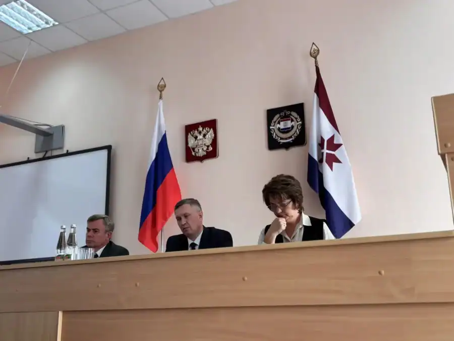 Трое участников заседания сидят за столом рядом с российским и региональным флагами.