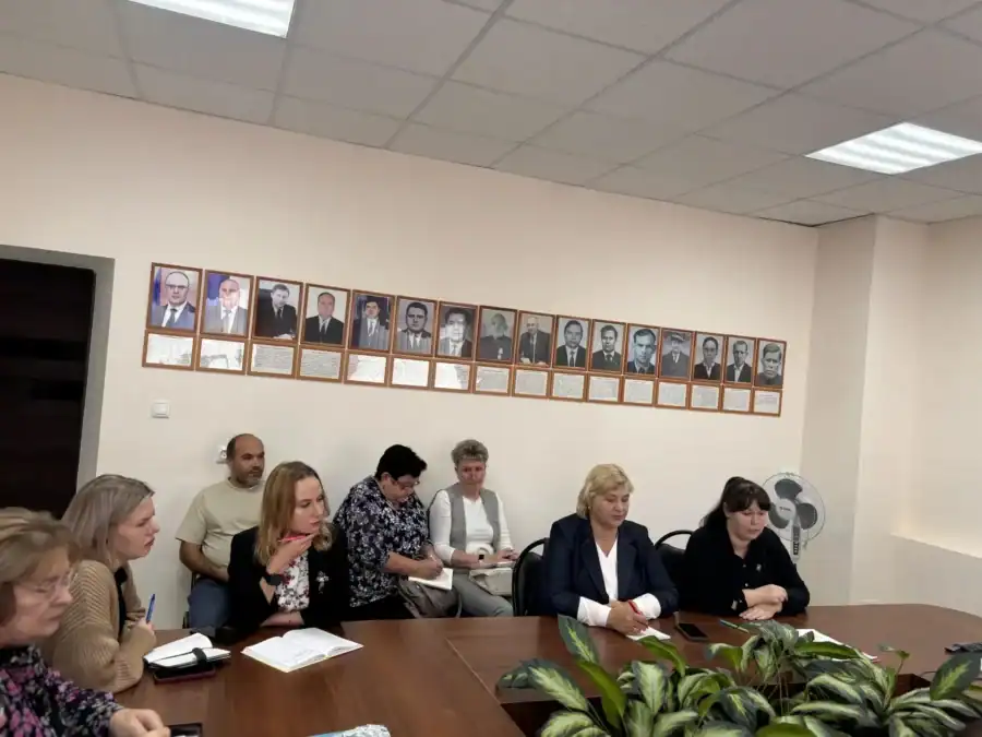 Участники заседания ведут записи за столом, на стене размещены портреты.