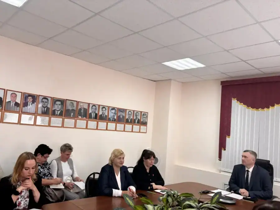Участники заседания сидят за столом напротив руководителя в кабинете.