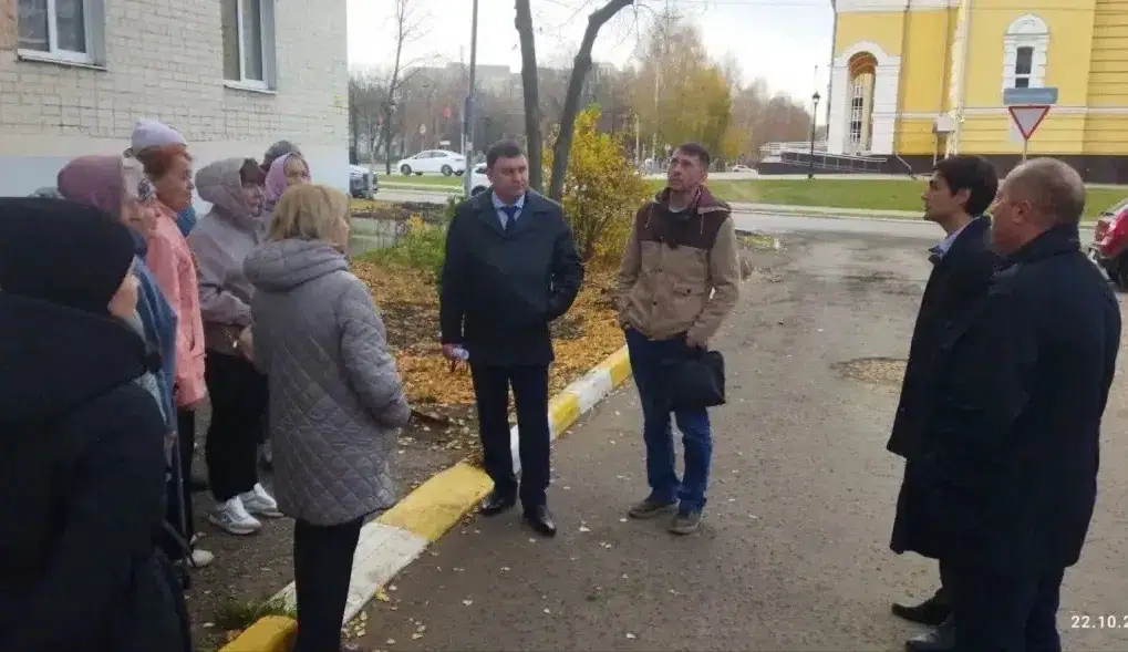 Группа жителей и мужчин в деловой одежде собралась у жилого дома.