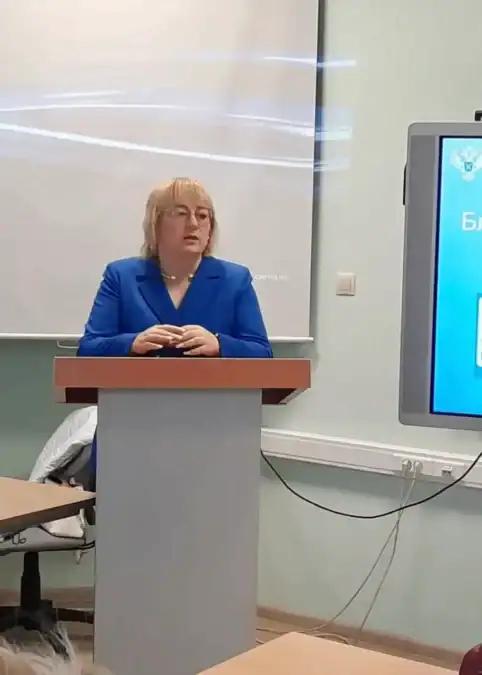 Женщина в синем пиджаке выступает за кафедрой рядом с экраном.