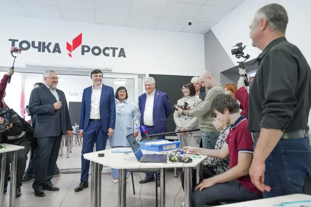 Группа взрослых осматривает учебное пространство «Точка роста» с робототехническим оборудованием.