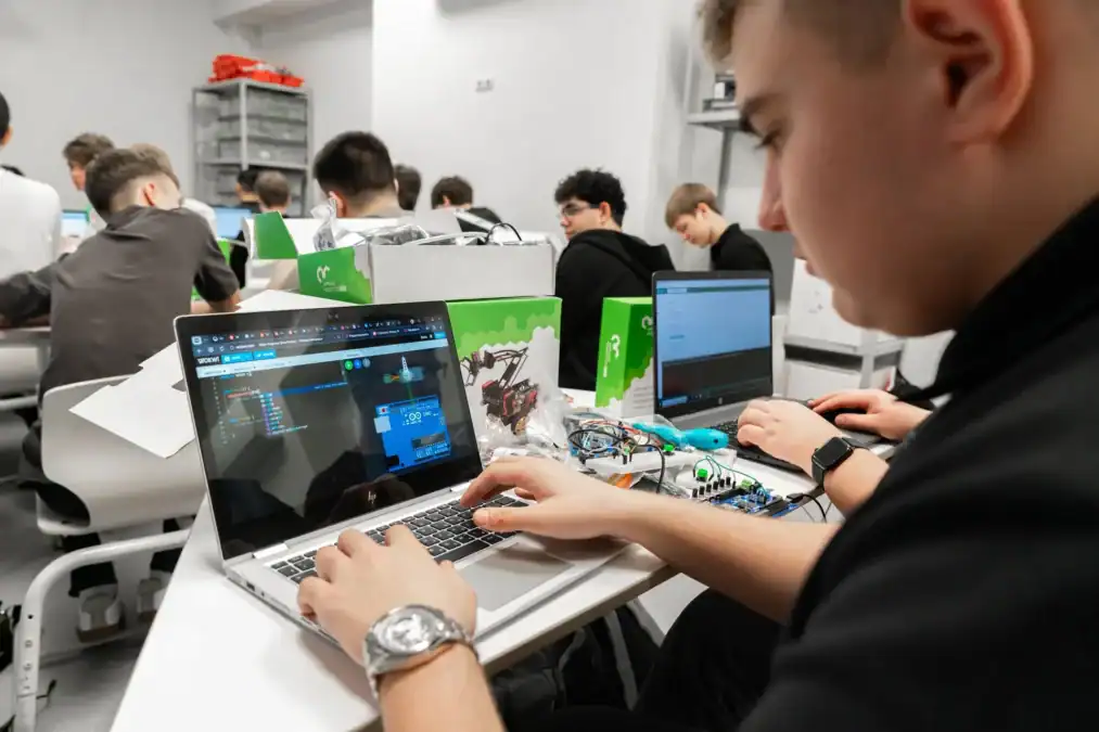 Подросток работает за ноутбуком и собирает электронное устройство в учебной лаборатории.