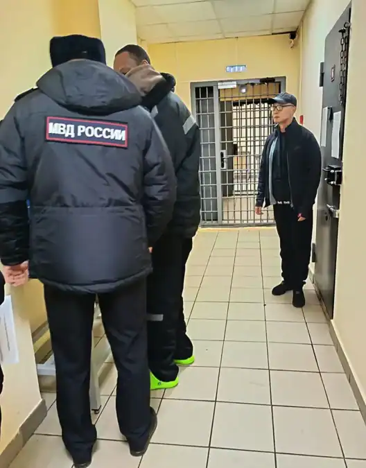 Сотрудники полиции и мужчина находятся в коридоре у решетчатой двери.