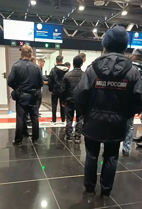Сотрудники полиции сопровождают мужчин в зоне паспортного контроля аэропорта.