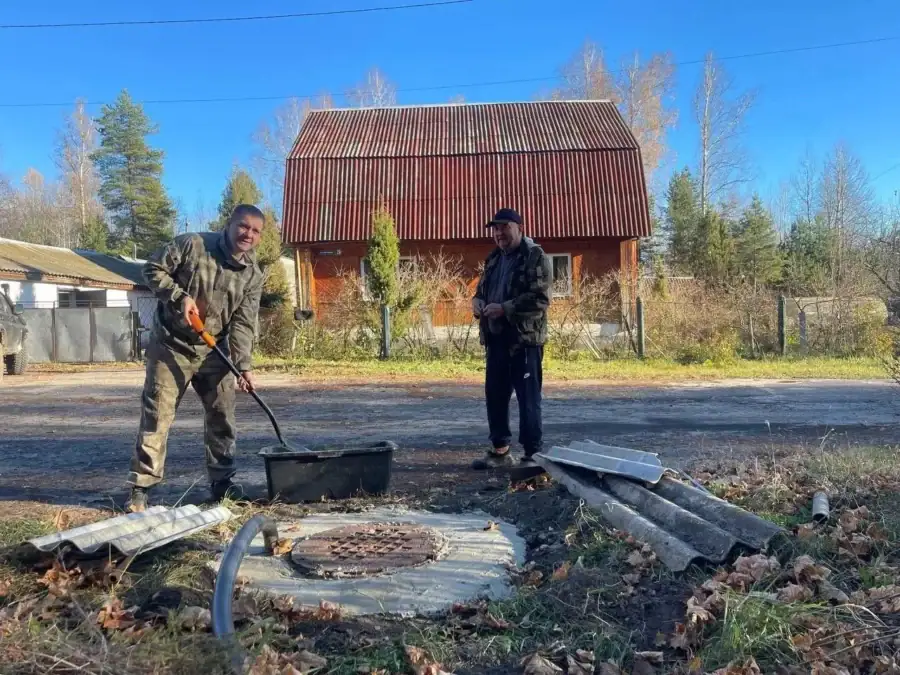 Двое мужчин убирают мусор на участке перед деревянным домом.