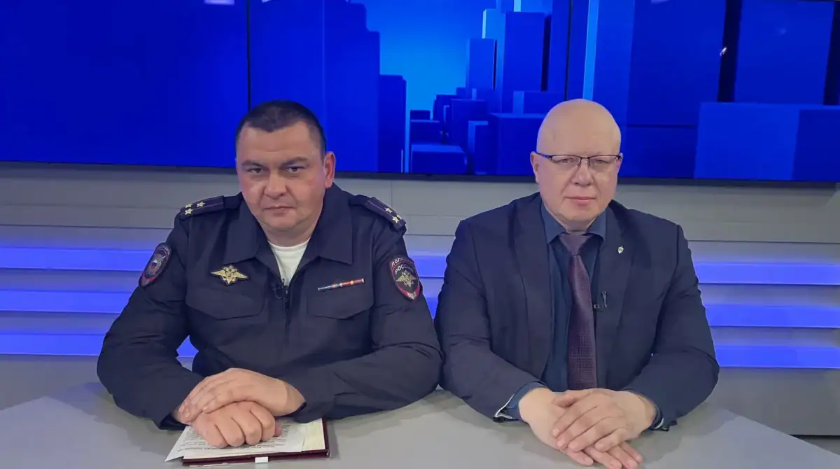 Двое мужчин, один в полицейской форме, сидят за столом в студии.