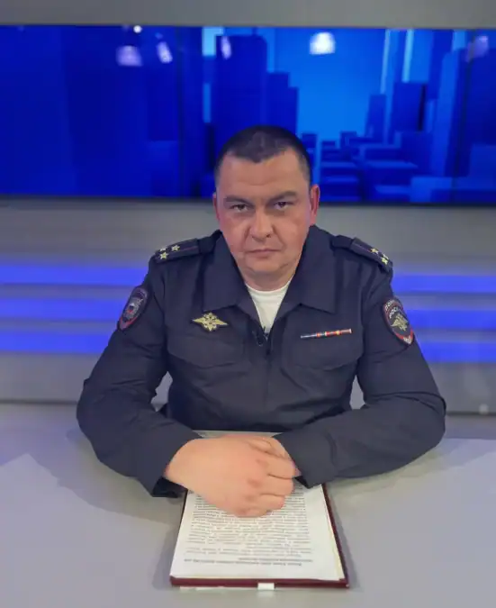 Сотрудник полиции в форме сидит за столом с папкой документов.
