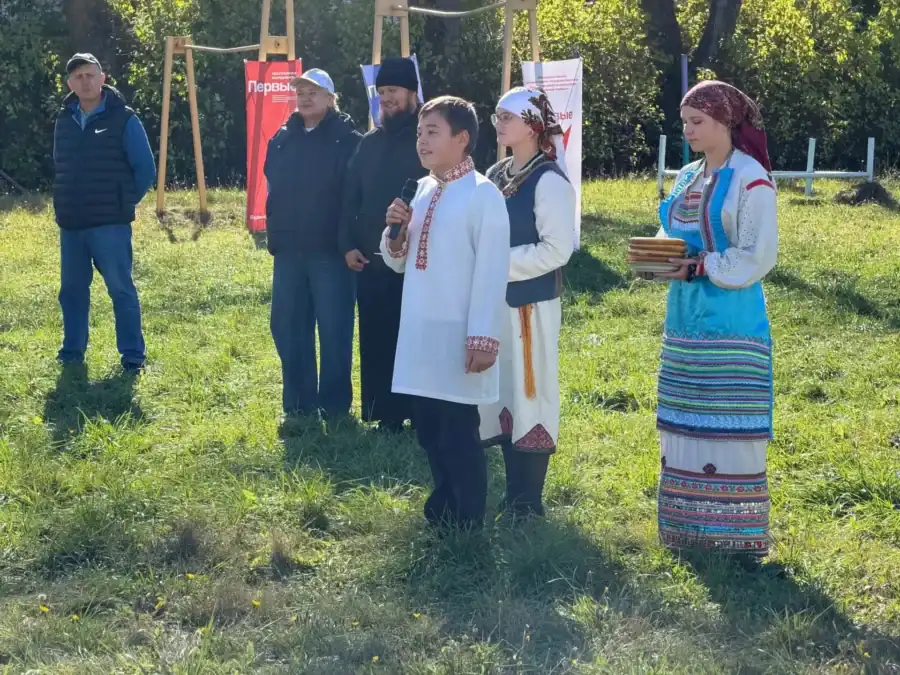 Участники в народных костюмах выступают перед собравшимися на траве.