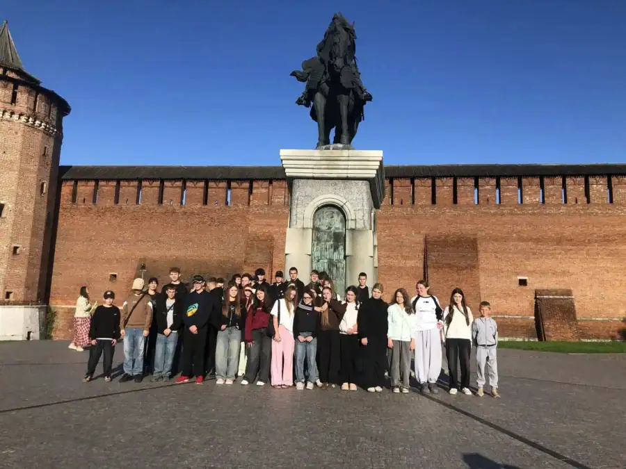 Группа школьников стоит у памятника на фоне кирпичной стены кремля.