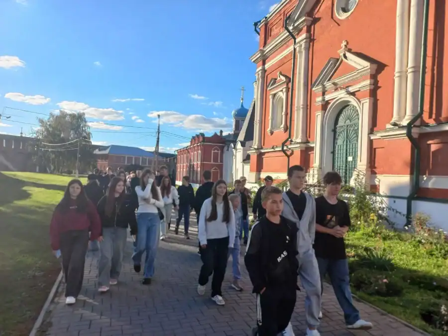 Школьники идут по тротуару рядом с краснокирпичным храмом.