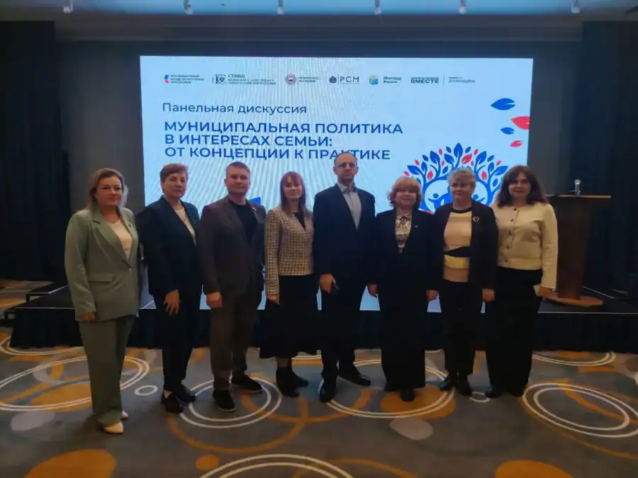 Восемь участников панельной дискуссии стоят перед экраном с названием темы.