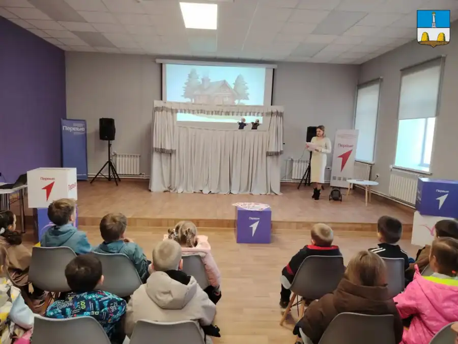 Дети смотрят кукольное представление на сцене с белой ширмой.