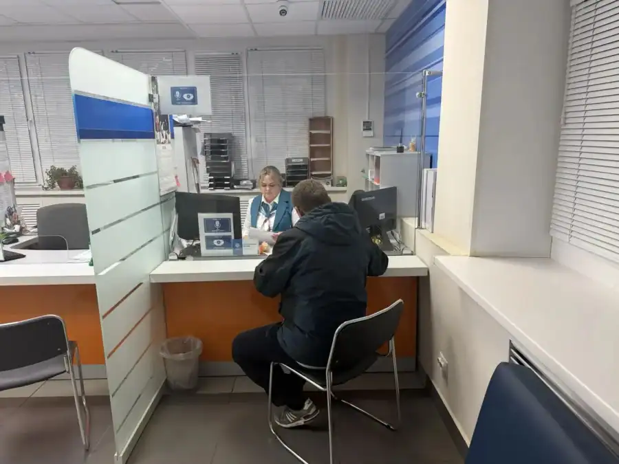 Посетитель сидит у окна напротив сотрудницы налоговой службы.