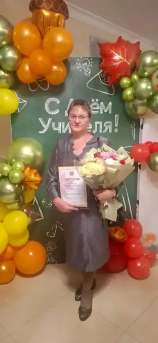 Женщина с дипломом и букетом стоит у праздничной фотозоны с воздушными шарами.