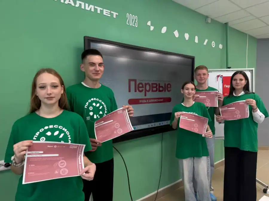 Пятеро молодых людей в зелёных футболках держат сертификаты в учебной аудитории.