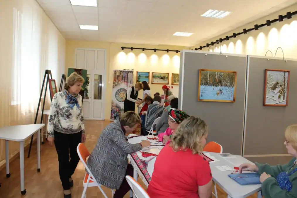Посетители занимаются рукоделием за столами в выставочном зале.