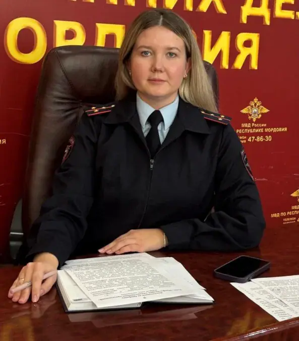 Сотрудница полиции сидит за столом с документами и телефоном.