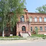Двухэтажное кирпичное историческое здание с арочными окнами и входной лестницей.