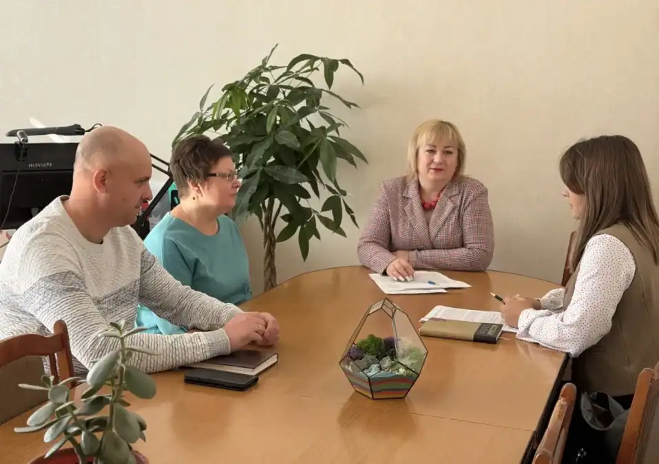 Четыре человека обсуждают документы за столом в офисе.